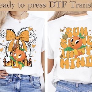 May include: White t-shirt featuring a front design with a cartoon orange character, castle, and bow. The back of the shirt has the text "Sun Shine In My Mind" with the same orange character. The words "Ready to press DTF Transfer" are at the top.