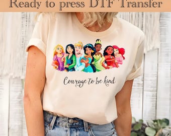 May include: A white t-shirt with a print of seven Disney princesses, including Cinderella, Ariel, Belle, Jasmine, Pocahontas, Mulan, and Tiana. The text "Courage to be kind" is printed below the princesses.