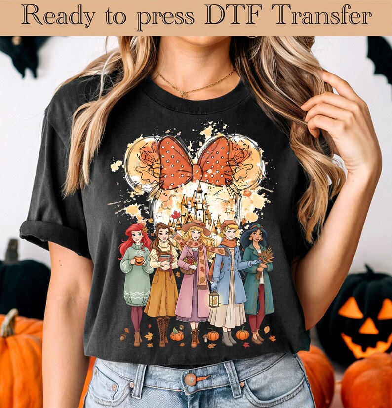 May include: Black t-shirt featuring a DTF transfer design. The design includes a large bow with polka dots, Mickey Mouse ears, a castle, and illustrations of Disney princesses in fall attire. The text "Ready to press DTF Transfer" is at the top.