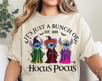 May include: Beige t-shirt featuring a graphic of three cartoon characters dressed as witches, with the text "IT'S JUST A BUNCH OF HOCUS POCUS EST. 1693". The design includes bats and stars.