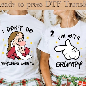 以下が含まれることがあります： お揃いのデザインの白いTシャツ。片方には漫画のキャラクターと「I DON'T DO MATCHING SHIRTS」の文字が、もう片方には漫画の手と「I'M WITH GRUMPY」の文字がプリントされています。