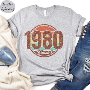 May include: Heather gray t-shirt with a vintage-style graphic of the year 1980 in a circle with a rainbow stripe design and the word "Classic" underneath.