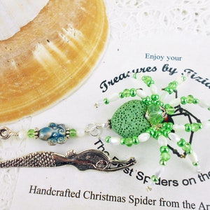 May include: Green and white beaded spider Christmas ornament with a green lava rock body. The spider is attached to a silver mermaid bookmark with a blue and white bead.