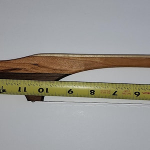 May include: A wooden cheese slicer with a curved handle and a stainless steel wire. The slicer is made of various wood tones, including light and dark brown. The handle measures approximately 28 cm in length.