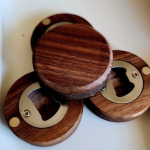May include: Three wooden bottle openers with a metal opener inset. The openers are round and have a dark brown wood grain.