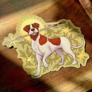 May include: A sticker featuring a dog with a sword in its mouth. The dog is white with brown patches and stands on a light green background with a yellow halo and stars. The sword is silver and the overall design has a vintage feel.