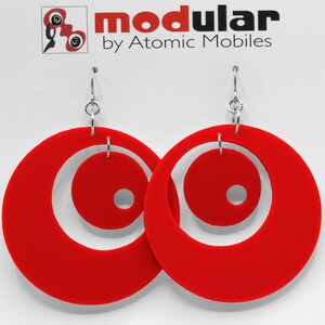 May include: A pair of red circular earrings with a smaller circle cut out of the center of each earring. The earrings are suspended from silver hooks.
