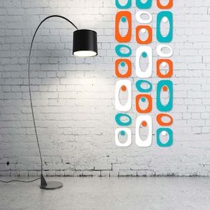 May include: A black floor lamp with a curved arm and a black shade illuminates a white brick wall with a decorative wall art design featuring a series of overlapping orange, white, and teal geometric shapes.