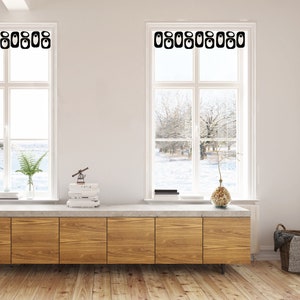 May include: Two white framed windows with black decorative accents above. The windows are set in a white wall. A wooden cabinet with a concrete top sits below the windows. The room has a hardwood floor. The windows look out onto a snowy landscape.