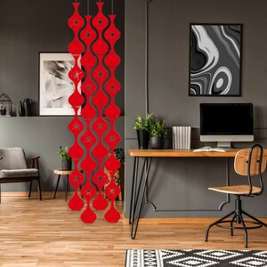 May include: Red, retro-style room divider with a repeating, wavy design. The divider features cut-out starburst patterns. The room is decorated with modern furniture, including a wooden desk, a gray chair, and artwork. The walls are painted a dark gray.