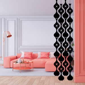 May include: A black, mid-century modern room divider with a repeating, wavy pattern. Each section features a starburst design. The divider hangs in front of a coral-colored sofa and a gold-toned coffee table.