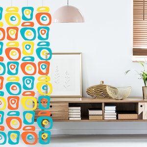 Può includere: Un muro bianco con un apparecchio di illuminazione appeso al soffitto. Uno scaffale in legno con libri e oggetti decorativi è montato sul muro. Il muro è decorato con un motivo geometrico colorato.