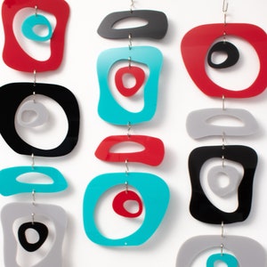 Pu&ograve; includere: Un mobile colorato fatto di cerchi e ovali in acrilico rosso, nero, grigio e turchese. Le forme sono sospese da una catena argentata.