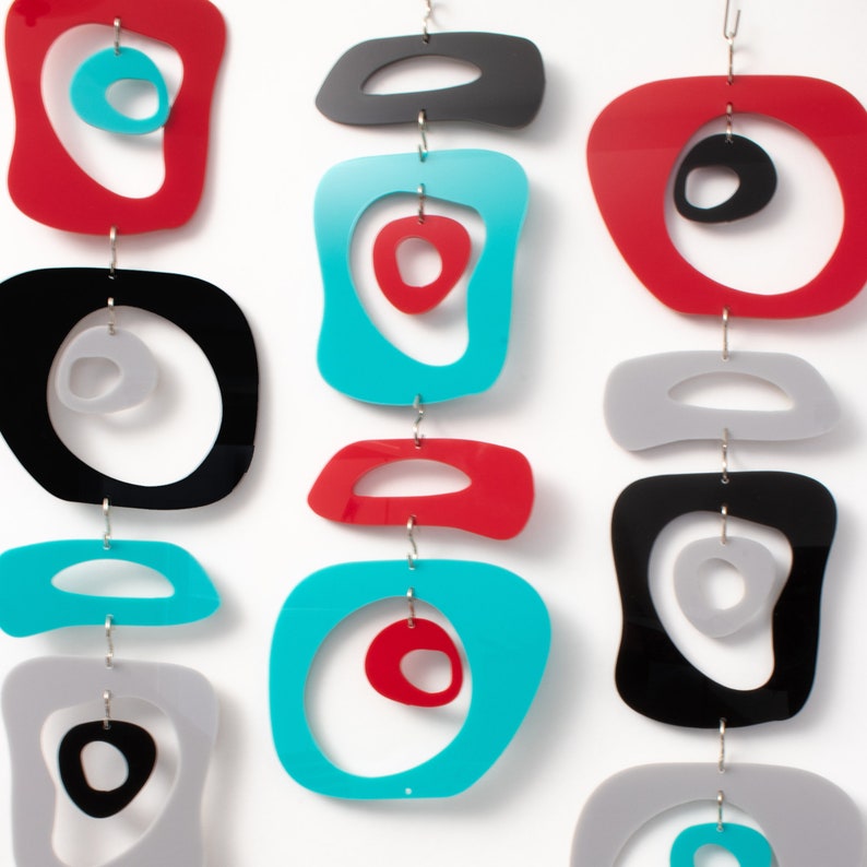 Pu&ograve; includere: Un mobile colorato fatto di cerchi e ovali in acrilico rosso, nero, grigio e turchese. Le forme sono sospese da una catena argentata.