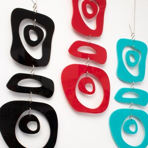 Pu&ograve; includere: Tre sculture mobili sospese con forme astratte. La scultura superiore &egrave; nera con un centro bianco, la scultura centrale &egrave; rossa con un centro bianco e la scultura inferiore &egrave; turchese con un centro bianco.