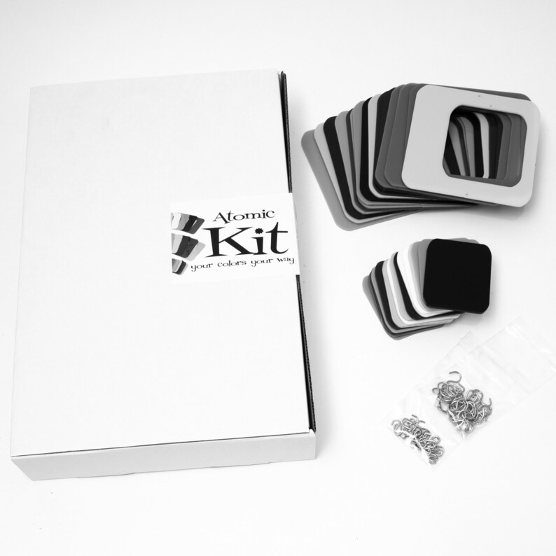 May include: A white box with the text "Atomic Kit your colors your way" on the side. The box contains a set of colorful squares, a set of black squares, and a bag of silver hooks.