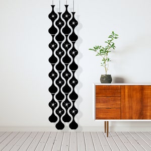 May include: Black, mid-century modern wall decor featuring a repeating pattern of stylized, elongated vase shapes with starburst accents. The decor hangs from thin cords against a white wall, with a wooden cabinet and plant in the background.