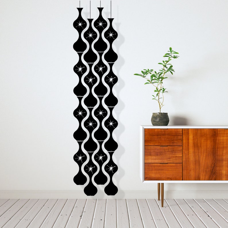 May include: Black, mid-century modern wall decor featuring a repeating pattern of stylized, elongated vase shapes with starburst accents. The decor hangs from thin cords against a white wall, with a wooden cabinet and plant in the background.