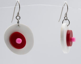 May include: A pair of white and red geometric earrings with pink accents. The earrings are made of acrylic and have a simple, modern design.