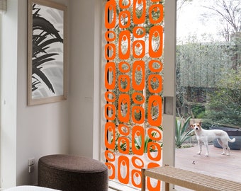 May include: Orange geometric shapes hang from a string in front of a window. The shapes are various sizes and are arranged in a repeating pattern. The window is open and shows a view of a backyard with a dog.