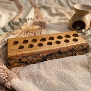 Könnte beinhalten: Ein rechteckiger Holzständer mit einer natürlichen Baumkante an der Vorderseite und einer glatten Oberfläche, in die vierzehn kreisförmige Löcher in zwei Reihen gebohrt sind. Die Holzmaserung ist sichtbar und zeigt einen hellbraunen Farbton.