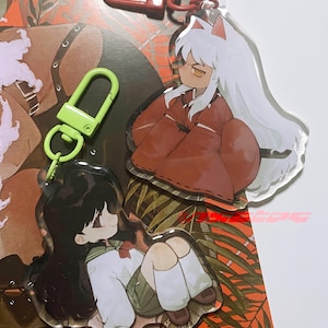 以下が含まれることがあります： InuYashaのアニメキャラクターのアクリルキーホルダー2つ。1つのキーホルダーは白い髪と赤い衣装のキャラクターが特徴です。もう1つのキーホルダーは黒い髪と制服のキャラクターが特徴です。どちらのキーホルダーも透明な背景で、赤と緑の留め金が付いています。