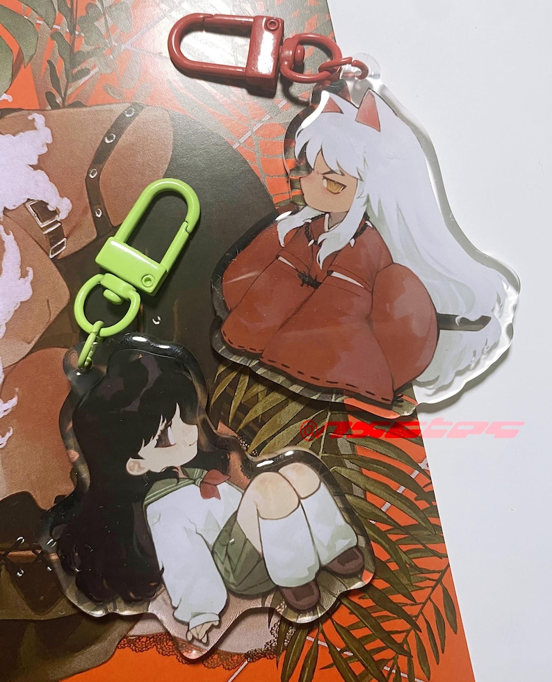 以下が含まれることがあります： InuYashaのアニメキャラクターのアクリルキーホルダー2つ。1つのキーホルダーは白い髪と赤い衣装のキャラクターが特徴です。もう1つのキーホルダーは黒い髪と制服のキャラクターが特徴です。どちらのキーホルダーも透明な背景で、赤と緑の留め金が付いています。