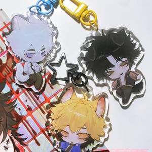 May include: A collection of anime-style character keychains. The keychains feature various characters with animal-like features, such as cat and fox ears, in different outfits. Each keychain has a colored clasp, including blue and yellow.