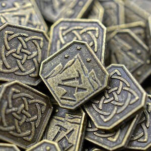 May include: Close-up of a pile of antique bronze-colored metal coins. The coins have a hexagonal shape with intricate Celtic knot and mountain designs. The coins are likely for a board game or collectible.