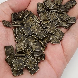 May include: A pile of small, square, bronze-colored metal tokens with different designs. Each token features a different image, including a skull and crossbones, a tree, and a building. The tokens are arranged in a random order.