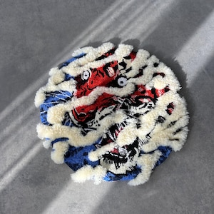 以下が含まれることがあります： 虎の模様が施された、丸い青、赤、黒の敷物。敷物は縁に白いふわふわのフリンジが付いている。