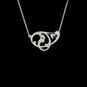 May include: A silver necklace with a delicate, openwork pendant. The pendant features a swirling, floral design with embedded clear gemstones. The necklace hangs on a fine chain against a black background.