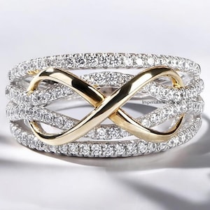 May include: A gold and silver infinity ring with a band of small clear stones. The infinity symbol is made of gold and is set on a silver band with a row of clear stones on each side.