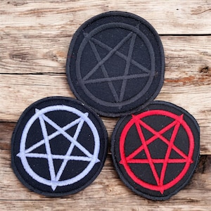 May include: Three circular patches featuring a pentagram design. One patch has a black pentagram on a black background, another has a white pentagram on a black background, and the third has a red pentagram on a black background. The patches are on a wooden surface.