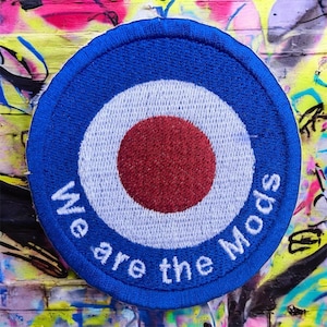 May include: Circular embroidered patch featuring a blue, white, and red bullseye design. The patch reads "We are the Mods" in white text. The patch has a blue border and is against a graffiti background.