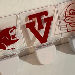 May include: Three clear plastic night lights with red vinyl designs. The first night light has a red dragon design. The second night light has a red "TV" design. The third night light has a red cartoon bird design.
