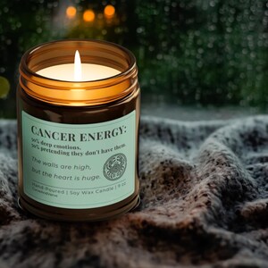 Cancer Zodiac Candle glowing warmly on a cozy knit blanket near a window. Light green label with humorous Cancer energy description, perfect for mindfulness and relaxation.