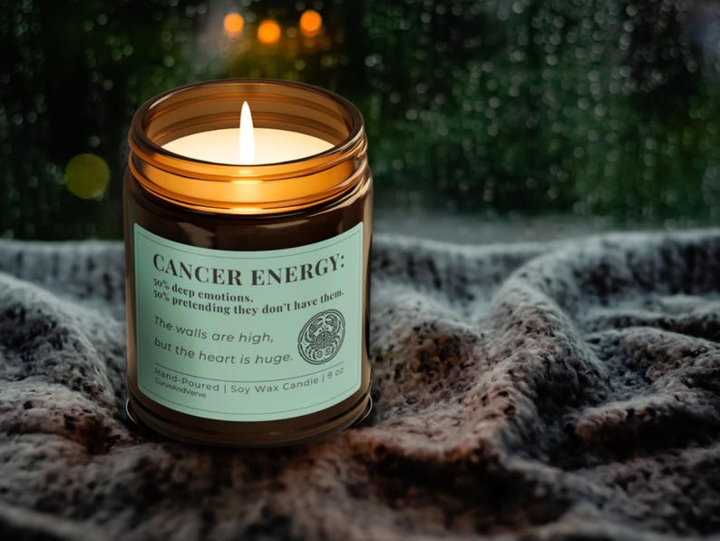 Cancer Zodiac Candle glowing warmly on a cozy knit blanket near a window. Light green label with humorous Cancer energy description, perfect for mindfulness and relaxation.