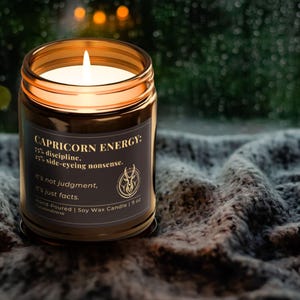 Capricorn Energy Candle glowing warmly in a cozy, ambient setting with a blanket backdrop, capturing the moody and sophisticated vibe.