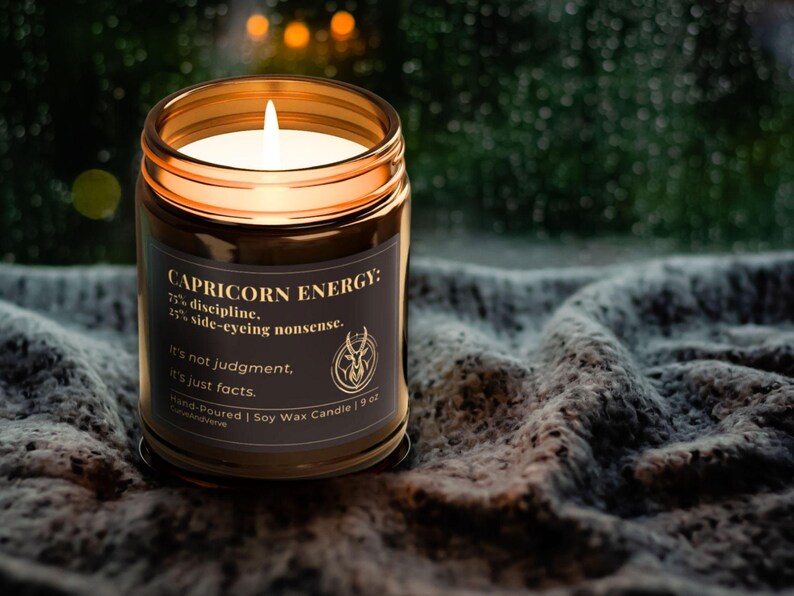 Capricorn Energy Candle glowing warmly in a cozy, ambient setting with a blanket backdrop, capturing the moody and sophisticated vibe.