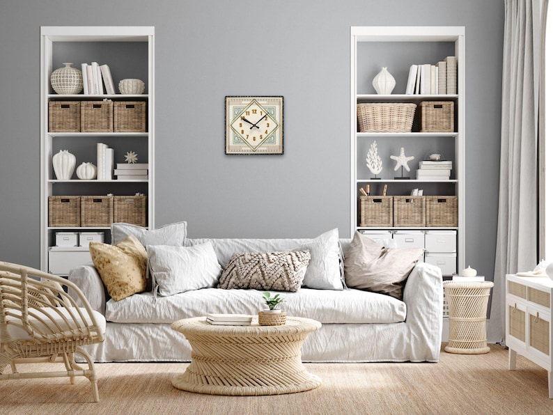 May include: A white couch with pillows and a woven coffee table in a living room with white shelves and baskets. A clock with a diamond shape and a cream background is on the wall.
