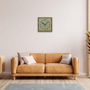 Art Deco wall clock styled above a mustard yellow couch with neutral décor and natural lighting.