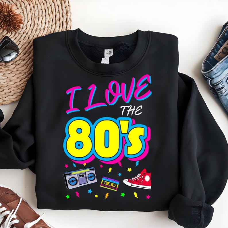 May include: Black sweatshirt with a graphic print of the text "I Love the 80's" in pink, blue, and yellow. The graphic also includes a cassette tape, a boombox, and a red high-top sneaker.
