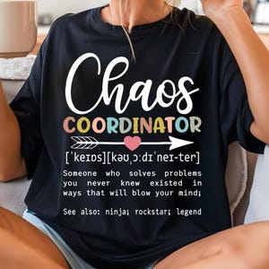 Może przedstawiać: Czarny T-shirt z białym tekstem, kt&oacute;ry brzmi "Chaos Coordinator" z definicją poniżej. Definicja brzmi: "['keips][kə ɔ:dı'nei-ter] Ktoś, kto rozwiązuje problemy, o kt&oacute;rych nigdy nie wiedziałeś, że istnieją, w spos&oacute;b, kt&oacute;ry rozsadzi ci m&oacute;zg; Zobacz także: ninja; rockstar; legenda"