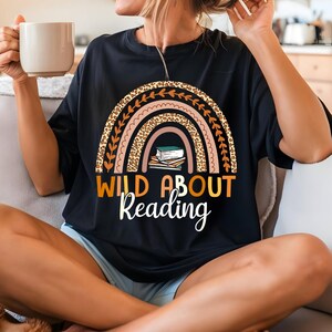 May include: Black t-shirt with a rainbow design featuring a leopard print and stacked books. The text "Wild About Reading" is printed below the rainbow.