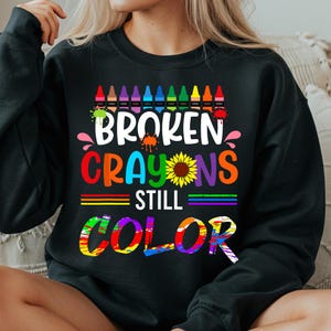 May include: Black sweatshirt with a rainbow of crayons, a sunflower, and the text "Broken Crayons Still Color".