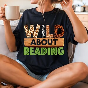 May include: Black t-shirt with the text "WILD ABOUT READING" in green and brown letters. The word "WILD" is made up of animal print patterns: leopard, zebra, giraffe, and tiger.