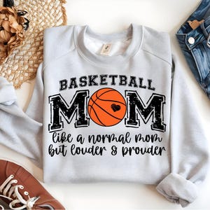Puede incluir: Sudadera gris con el texto "Basketball Mom like a normal mom but louder & prouder" y un gráfico de baloncesto.