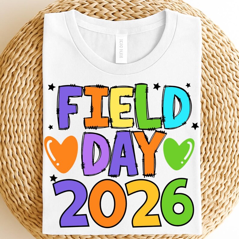 May include: White t-shirt with a colorful graphic that reads "FIELD DAY 2026". The text is in various colors, including yellow, green, blue, orange, and purple, with black outlines. The design includes hearts and stars.