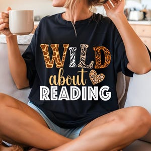 May include: Black t-shirt with the text "WILD about READING" in white letters. The letters are decorated with animal print patterns in orange, brown, and white.